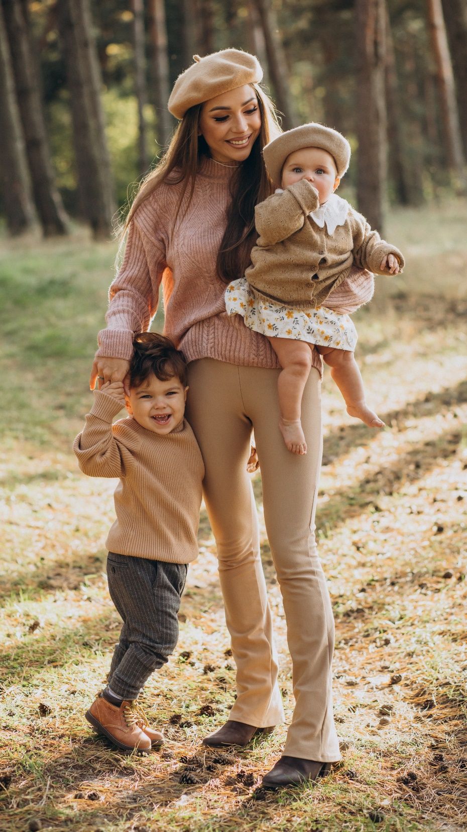 A mother carrying her baby while walking with her toddler through an autumn forest